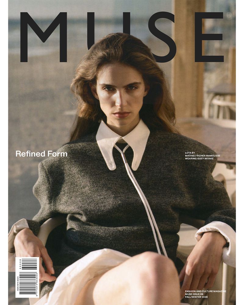 Model wearing dark grey wool sweater and white collared shirt against a blurred outdoor cafe background