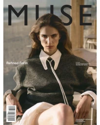 Model wearing dark grey wool sweater and white collared shirt against a blurred outdoor cafe background