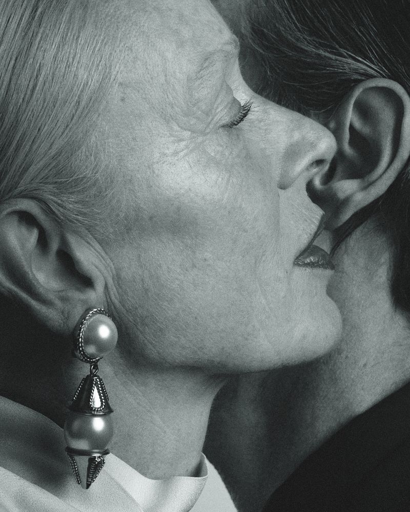 Close-up portrait in monochrome of an older woman wearing large pearl drop earrings leaning in near another person