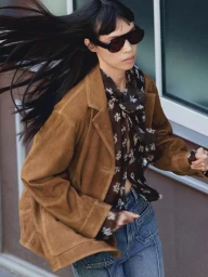 Model in brown suede jacket with dark sunglasses and blowing hair outdoors