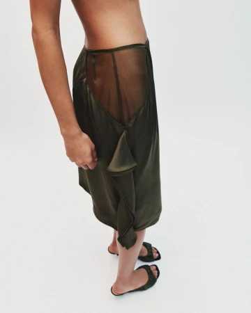 Model wearing dark olive green sheer panel skirt and matching sandals against white seamless background