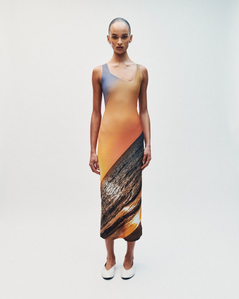 Model standing against a white seamless background wearing a gradient sleeveless midi dress and white shoes.