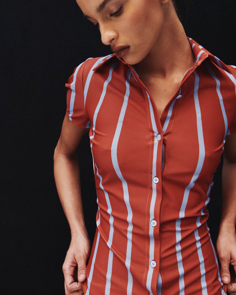 Model wearing a rust orange button-up shirt with light blue vertical stripes against a black background
