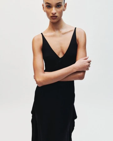 Model in a black sleeveless dress standing against a plain white studio background.