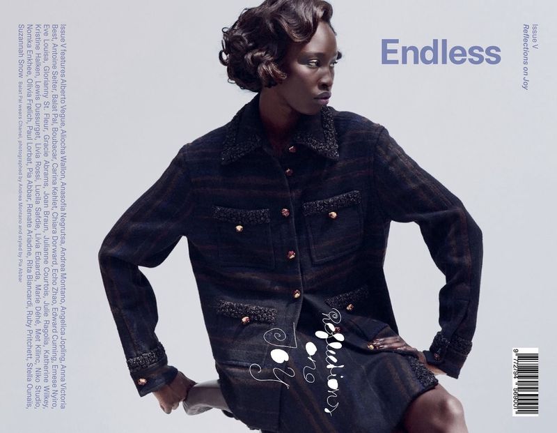 Black model with styled short hair wearing dark tweed textured jacket against neutral grey background