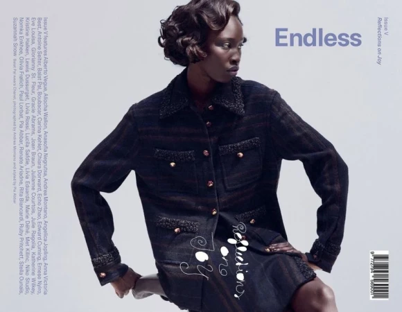 Black model with styled short hair wearing dark tweed textured jacket against neutral grey background