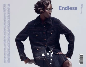 Black model with styled short hair wearing dark tweed textured jacket against neutral grey background