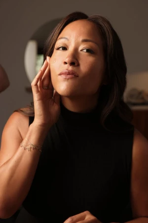 Woman in a black top applying skincare serum to her face for La Mer The Concentrate Confessions campaign.