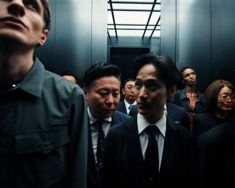 Group of diverse people in business attire and dark shirts standing inside a modern elevator with vertical metal panels