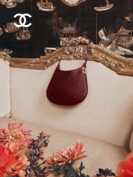 Burgundy quilted leather hobo bag hanging on an ornate vintage sofa with floral arrangements in foreground