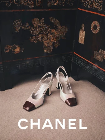 Two-tone slingback heels with dark cap toes placed on a beige carpet against a dark lacquered folding screen with gold floral motifs.