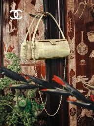 Chanel light green quilted leather handbag hanging from an ornate dark wooden door against a patterned lacquered screen.