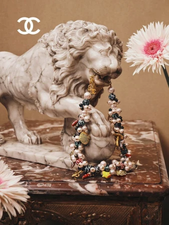 Marble lion statue holding a pearl and charm necklace in its mouth on a table with flowers.