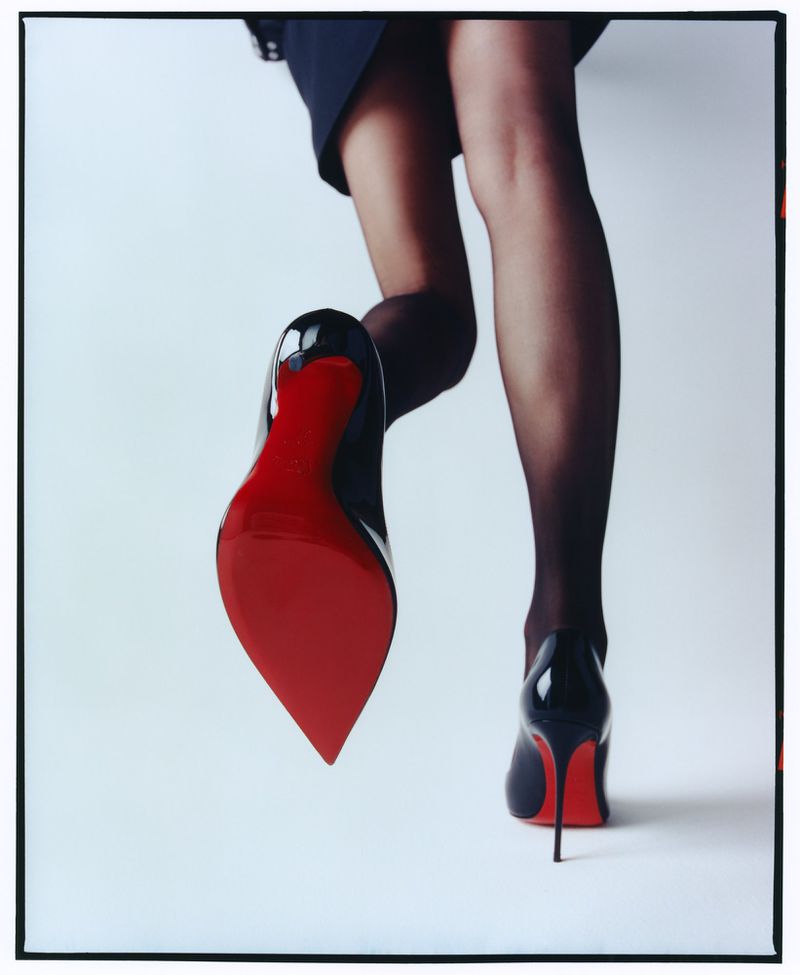 Low angle shot of woman in black tights wearing red sole high heels against a white seamless background