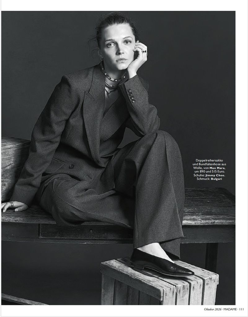 Model seated on a wooden table wearing a dark grey oversized suit jacket and trousers for Madame Germany.