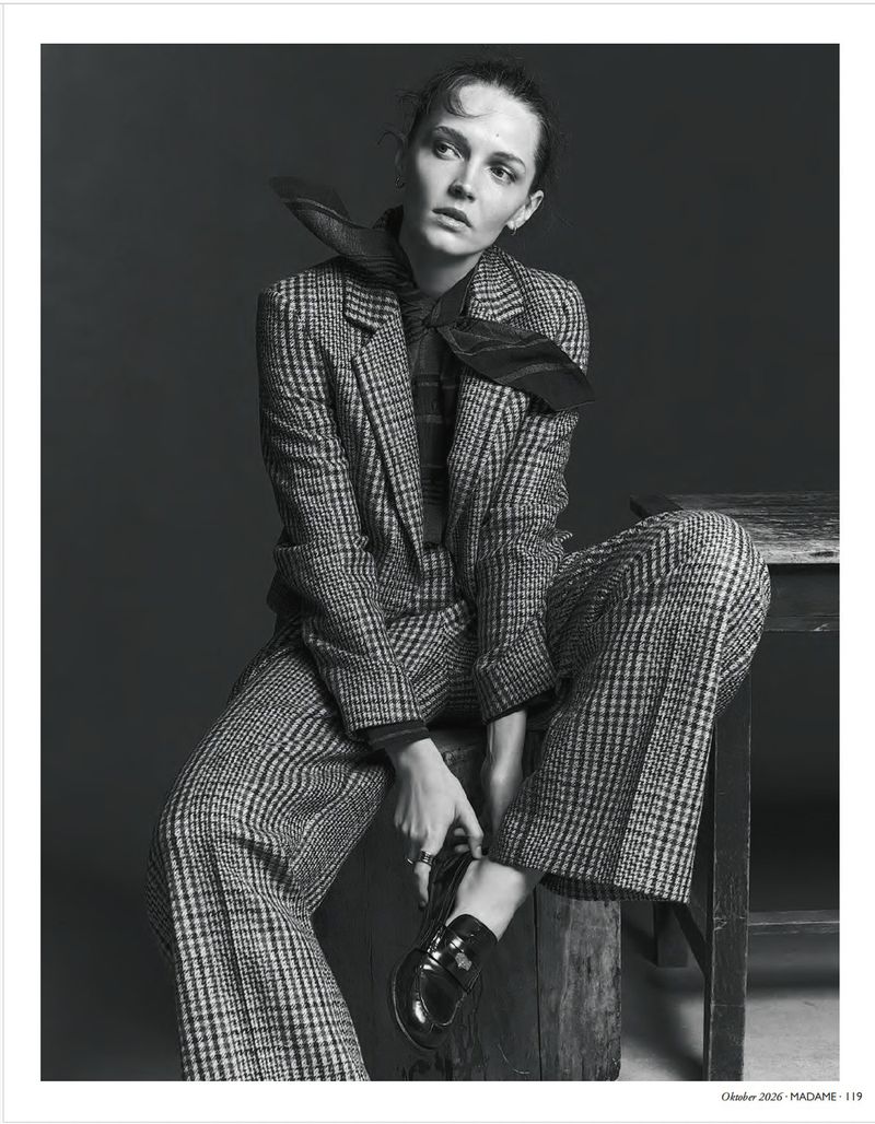 Model wearing a plaid pantsuit and necktie sitting on a wooden block in a monochrome fashion editorial portrait