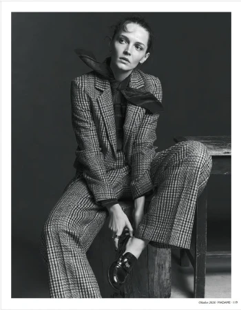 Model wearing a plaid pantsuit and necktie sitting on a wooden block in a monochrome fashion editorial portrait