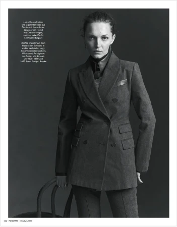 Black and white editorial portrait of a woman wearing a tailored double-breasted suit jacket against a dark studio background.