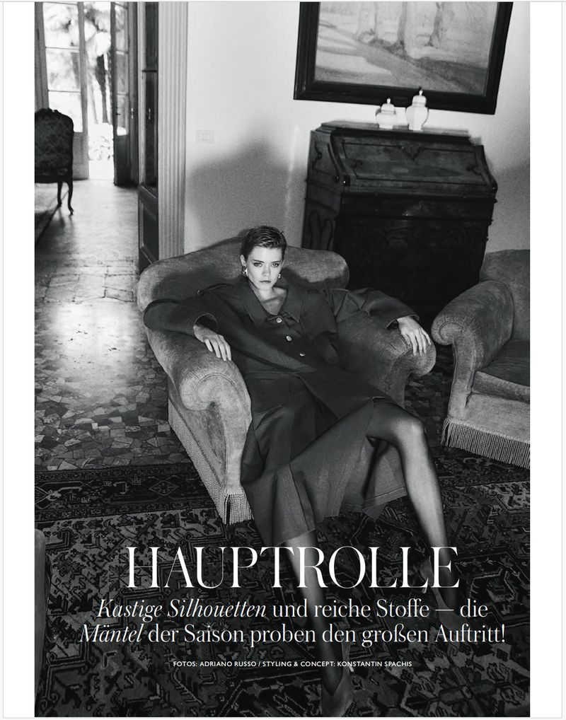 Model seated in an armchair in an interior room wearing a dark coat for Madame Germany editorial shot by Adriano Russo