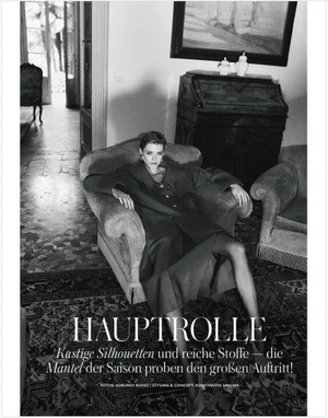 Model seated in an armchair in an interior room wearing a dark coat for Madame Germany editorial shot by Adriano Russo