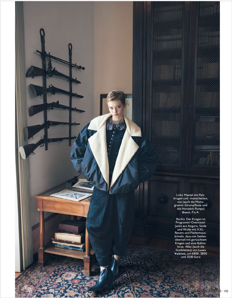 Model standing in a wood-paneled room wearing an oversized bomber jacket with a wide cream collar and dark trousers.