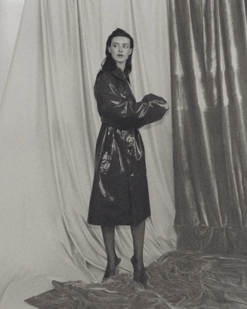 Portrait of actor Daisy Edgar-Jones in a glossy trench coat standing against draped fabric backdrops for Vogue España.