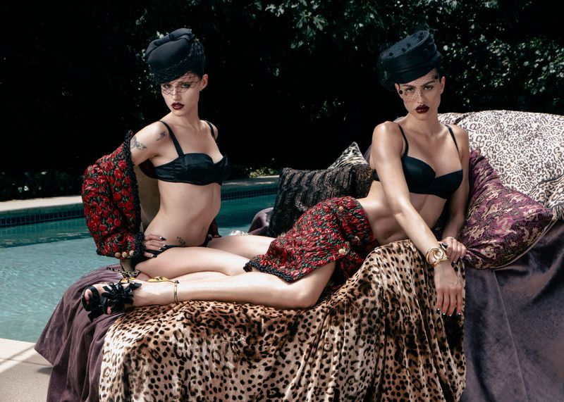 Two models wearing black bras and patterned skirts reclining by a swimming pool for Allure Magazine.