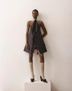 Model Agel Akol in a structured dark dress and knee-high socks standing on a white pedestal