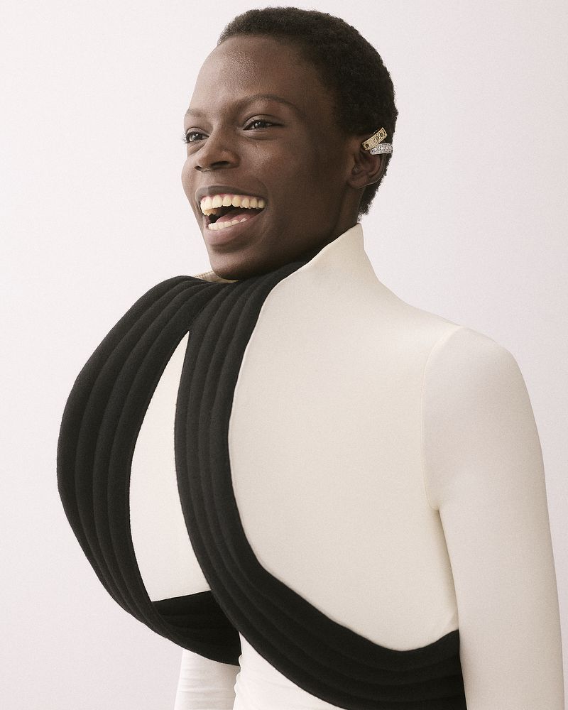 Model smiling wearing white top with large black padded structural neckpiece and ear cuffs