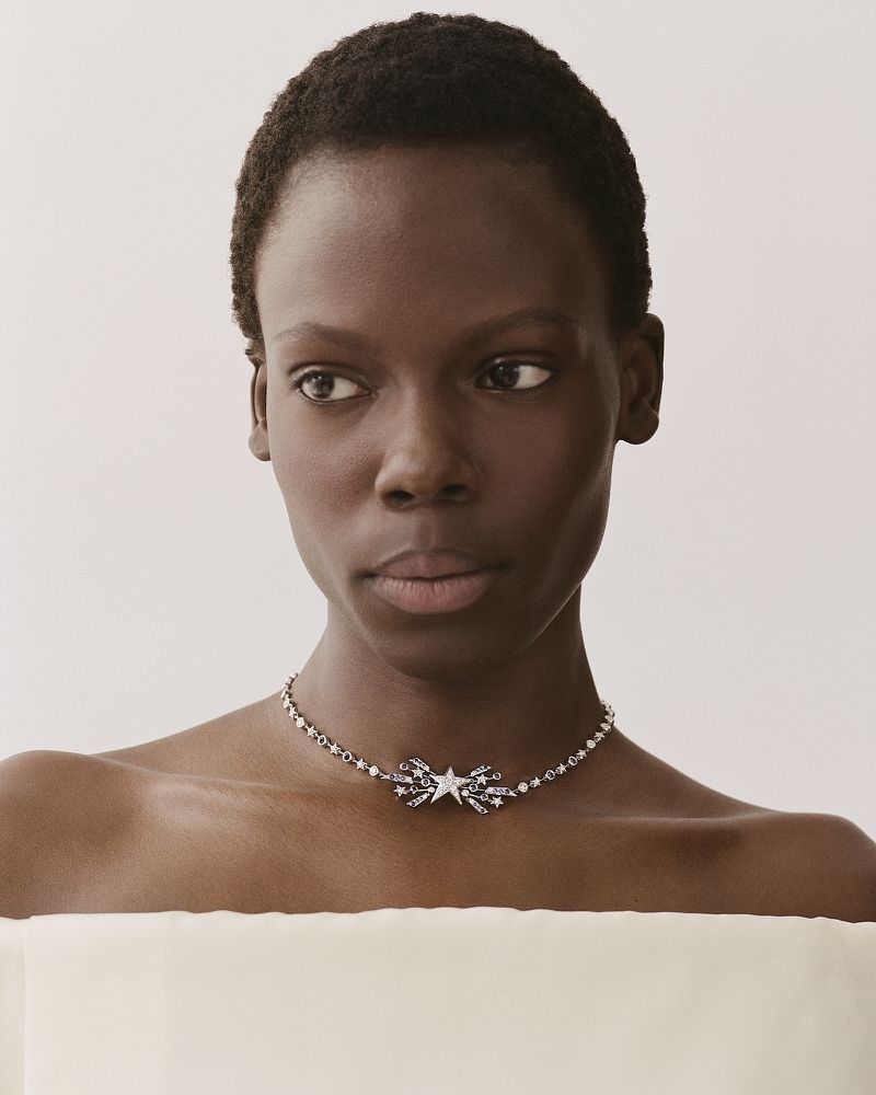 Model Agel Akol wearing a star-embellished silver necklace against a plain off-white studio background for Heroine Magazine.
