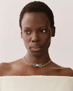 Model Agel Akol wearing a star-embellished silver necklace against a plain off-white studio background for Heroine Magazine.