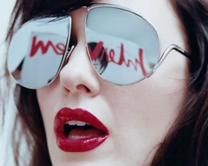 Close-up portrait of Rachel Brosnahan wearing reflective aviator sunglasses and glossy red lipstick.