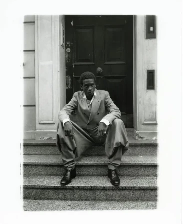 A black man in a double-breasted suit seated on stone steps before a dark wooden door for Financial Times HTSI Magazine.