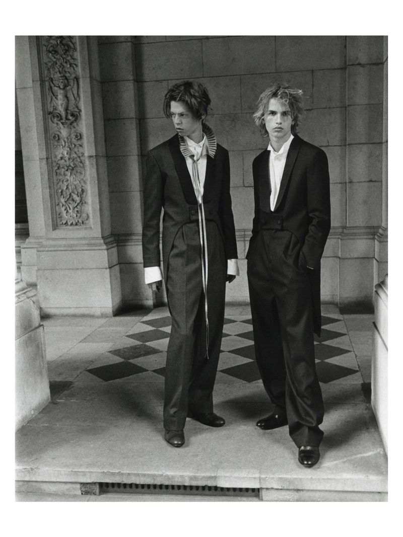 Two young male models wearing tailored suits standing in a stone-columned arcade for a Financial Times HTSI Magazine editorial shoot