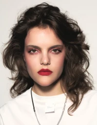 Close up portrait of a woman with dark wavy hair wearing bold red lipstick and a white t shirt against a seamless background