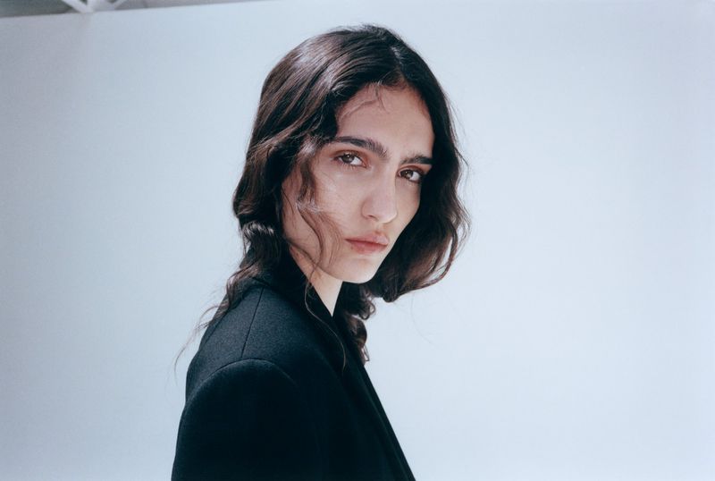 Close-up portrait of model Sara Caballero wearing a black blazer against a light background by Cornelius Kaess for Muse Magazine.