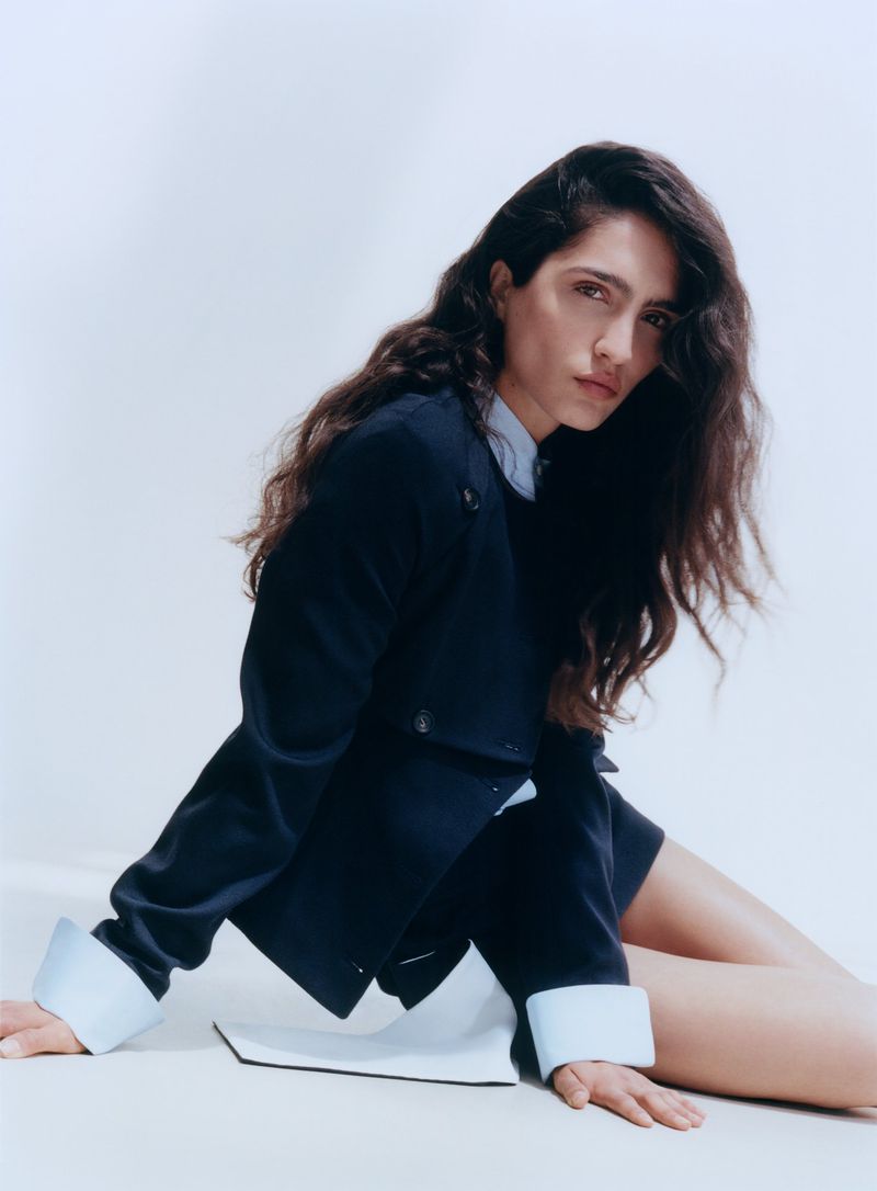 Model Sara Caballero in a dark jacket and pale cuffs posing against a white background for Muse Magazine