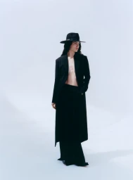 Model Sara Caballero wearing a black coat and hat against a white seamless background for Muse Magazine