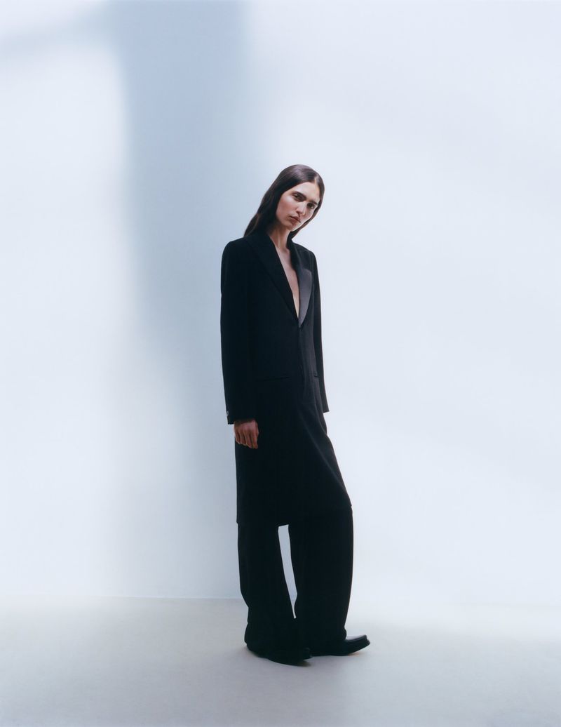 Full-length portrait of model Sara Caballero wearing a black tailored coat against a minimalist white background