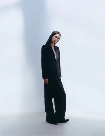 Full-length portrait of model Sara Caballero wearing a black tailored coat against a minimalist white background