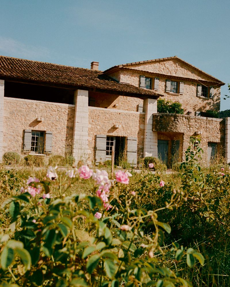 Stone farmhouse with tiled roof and open porch behind a field of pink and white flowers for WSJ