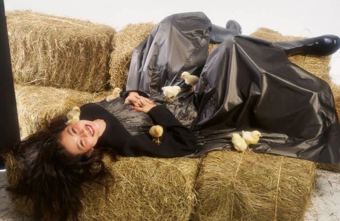 Hoyeon Jung lying on hay bales in a metallic coat surrounded by baby chicks for AnOther Magazine