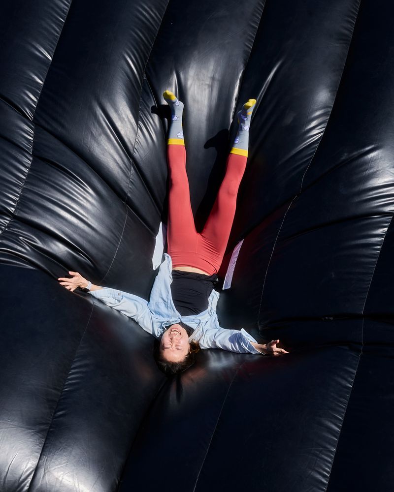 Smiling woman in red leggings and light blue shirt lying upside down on an inflated black stunt bag