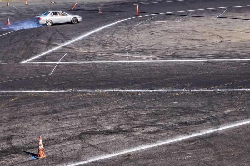 Silver sedan drifting on an asphalt training track with white line markings and orange cones