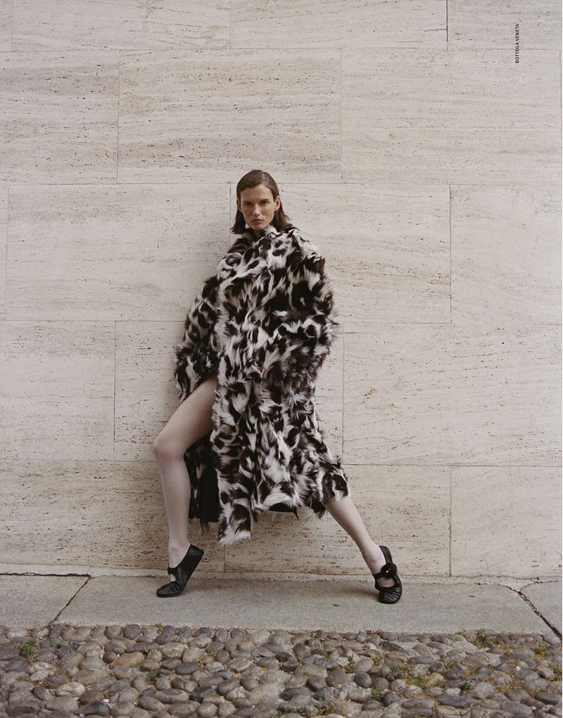 Giedre Dukauskaite wearing a black and white patterned coat against a stone wall for Love Want Magazine.