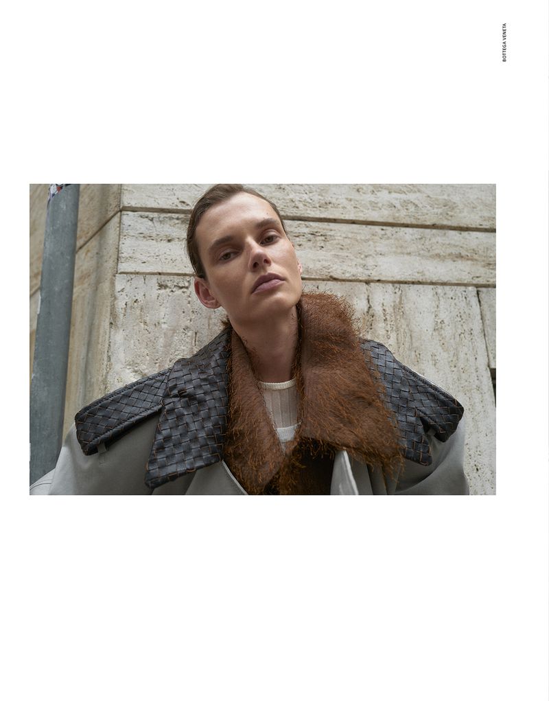 Model Giedre Dukauskaite wearing a structured jacket with a brown faux fur collar against a stone building exterior.