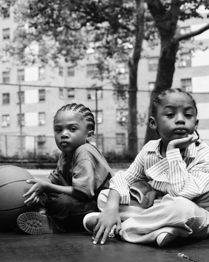 Two young children sitting outdoors on an urban basketball court next to a basketball, photographed by Luis Alberto Rodriguez for Zara.