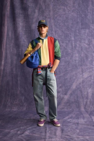 Model wearing a color-blocked rugby shirt and blue jeans standing against a purple textured backdrop for Zara.