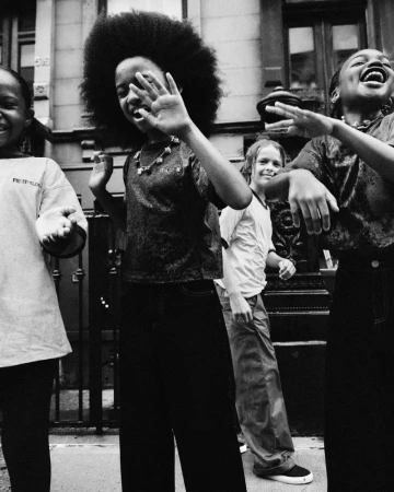 Black and white portrait of a group of four diverse young models laughing and dancing outdoors on a city sidewalk.