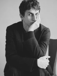 Man wearing dark tailored blazer resting chin on hand against a plain studio backdrop for Massimo Dutti